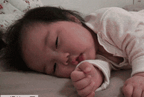 Video gif. A sweet, sleepy baby drowsily drifts off to sleep.