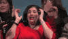 Video gif. Woman in a bright cherry red dress and matching lipstick runs her hands through her hair and screams in panic. Other women behind her are wiping away tears and blowing their noses, and snow begins to fall upon them.