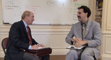 Movie gif. Sitting in a room with notes on their lap, Sasha Baron Cohen as Borat initiates a high-five with Pat Haggerty and laughs, then they quickly re-focus.