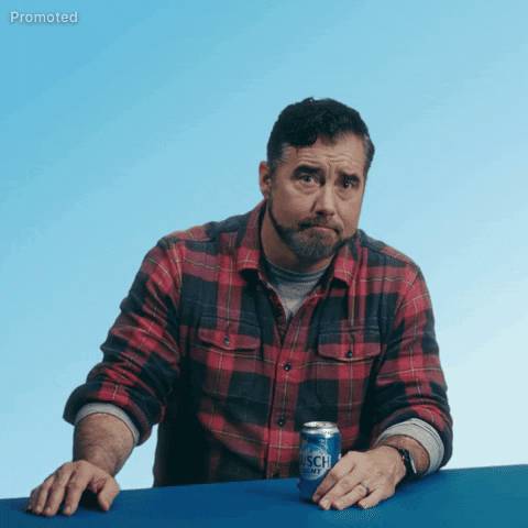 Sponsored gif. Gerald Downey in a red and black plaid shirt leans on a shelf as he lifts and points at a can of Busch Light beer, furrowing his brow and looking at us with a genuine expression like he's asking the quesiton that appears on screen, "Need a beer?"