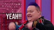 Reality TV gif. A person from Rupaul's Drag Race with short purple hair throws their hands up and shouts with excitement. Text, "Yeah!!"