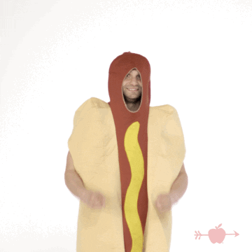 Video gif. A man in a giant hot dog costume raises his arms and crosses his fingers like he's wishing for something.