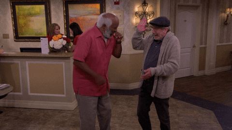 TV gif. David Alan Grier as Hank in "The Cool Kids" laughs and covers his mouth while high-fiving Martin Mull as Charlie.