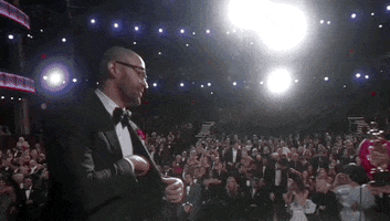 Oscars 2024 GIF. Cord Jefferson, taking the stage, ignores the Oscar being presented to him to greet presenter Melissa McCarthy with a big hug.