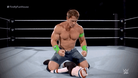 Sports gif. John Cena, a WWE wrestler, is in the ring and sits on top of a doll. He looks down at his hands and back at the doll, shocked at his strength and what he's done.