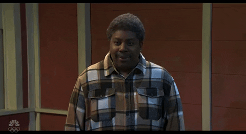 Video gif. Saturday Night Live castmember Mikey Day and guest host Ryan Gosling are dressed as Beavis and Butt-head for a sketch. Day and Gosling are sitting in the front row of a talk show audience. The two of them are staring straight ahead with goofy smiles on their faces. 