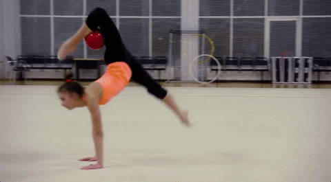 ginástica em espanhol

DESCRIÇÃO DA IMAGEM: Uma ginasta rítmica está fazendo exercícios com uma bola vermelha. 