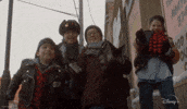 Disney gif. Four boys in The Mighty Ducks: Game Changers give each other five and celebrate as they stand together in winter gear on a city street.