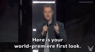 Video gif. On the 2024 Summer Game Fest stage, presenter Geoff Keighley, wearing a dark gray button-down shirt over a light gray t-shirt, holds a microphone in his right hand and says, 'Here is your world premiere fist look.' The caption at the bottom of the gif reads the same.