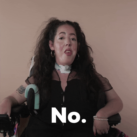 Reaction gif. A Disabled white woman with muscular dystrophy with wavy brown half up half down with two pigtails on top, seated in her motorized wheelchair, evades eye contact saying, "No."