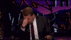 TV gif. James Cordon on The Late Late Show is sitting at his desk and has his hands on his face, pinching his eyes in annoyance.