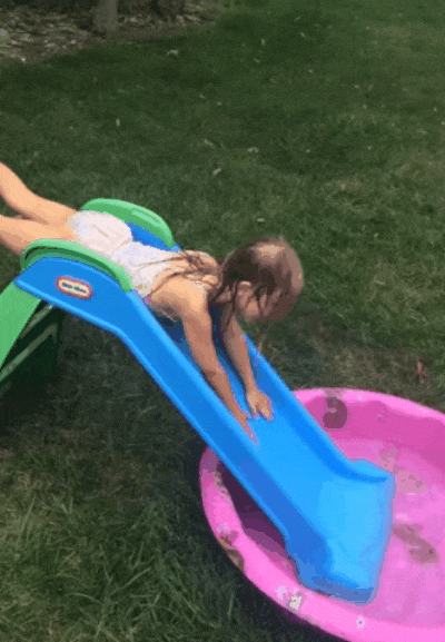 Video gif. Two toddlers are playing with a small slide that leads to an even smaller kiddie pool. The first child slides down on her tummy and lands in the pool but the other jumps off the slide and faceplants into the grass.