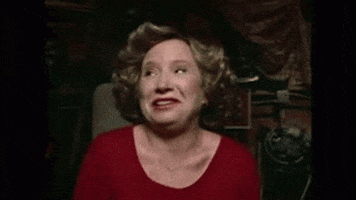 TV gif. Debra Jo Rupp as Kitty in That's 70s Show. She's high and in the basement sitting in the circle with everyone. She dissolves into laughter as she starts to giggle then folds over, laughing even harder.