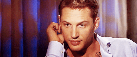 Celebrity gif. Tom Hardy looks up at us with a sexy gaze as he holds his hand near his ear. He then winks at us flirtatiously.