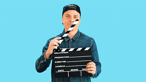 Video gif. A man shuts a movie clapper board and rolls his finger in a 360, saying, "That's a wrap!"