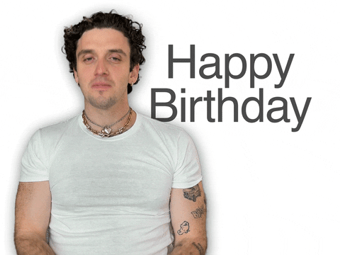 Video gif. Man with tattoos wearing a lot of chain jewelry gestures towards us and says, "Happy birthday" in a sincere yet casual and matter of fact way. 