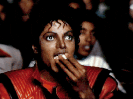 Meme gif. Michael Jackson in his Thriller jacket, sitting in a movie theater, eyes on the show, eating popcorn and grinning.