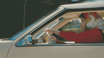 Music video gif. From the video for Raising Hell, Kesha drives fast in an old-fashioned car, appearing to be in a rush.