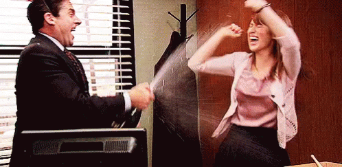 The Office gif. Steve Carrell as Michael Scott shakes and sprays a bottle of champagne at Ellie Kemper as Erin as she waves her arms and cheers excitedly.
