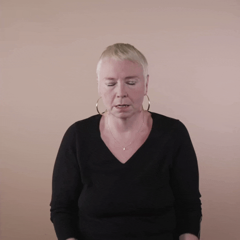 Reaction gif. A white woman with invisible disabilities, with hair styled in a sleek platinum pixie cut and big hoop earrings throws her hands to her face and shakes her head, exasperated.