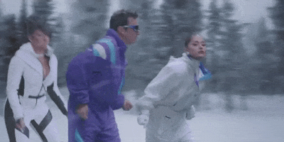 Music video gif. From the video for "It Was a Masked Christmas," Megan Thee Stallion, Jimmy Fallon, and Ariana Grande are wearing ski suits, shimmying their shoulders and leaning back.