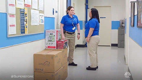 TV gif. Lauren Ash as Dina and Kaliko Kauahi as Sandra in Superstore. They're chatting in a hallway and Dina gets upset, turning away and kicking over a pile of boxes. She stomps on the boxes as she marches away.