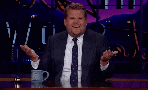 TV gif. James Corden on The Late Late Show sitting at his desk, palms facing up in a shrug, scrunches his eyebrows, and looks around in confusion, saying, "What?"