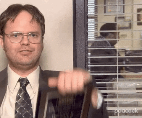 The Office gif. Rainn Wilson as Dwight holds up two February "Employee of the Month" plaques on either side of his face, looking miffed.