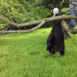 Video gif. A person dressed as Voldemort from Harry Potter waves their arms as they skip happily through a grassy field.