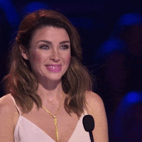 Reality TV gif. X Factor judge Dannii Minogue smiles and nods approvingly as she watches a contestant.