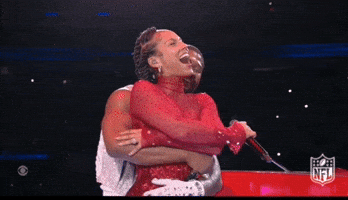 Celebrity gif. Alicia Keys and Usher embrace on stage at the Super Bowl halftime show. Usher gives Alicia a back hug and she closes her eyes and laughs with her mouth open.