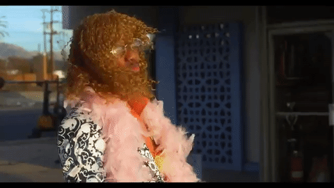 Celebrity gif. Nick Cannon, dressed lazily in drag, throws his hand to his brow, making a show of shading his eyes from the light, looking into the distance.
