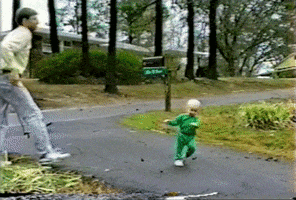 Video gif. Baby is in a driveway and they fall, catching themselves on their hands. They can't find their center of balance and they do a handstand as they begin to flip over.