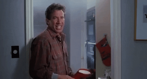 Movie gif. Tim Allen as Scott from The Santa Clause. He grimaces at us and holds a mitt sheepishly while a fire starts on the stove in the background. He's trying to convince us that he has the situation under control, but the fire says otherwise.