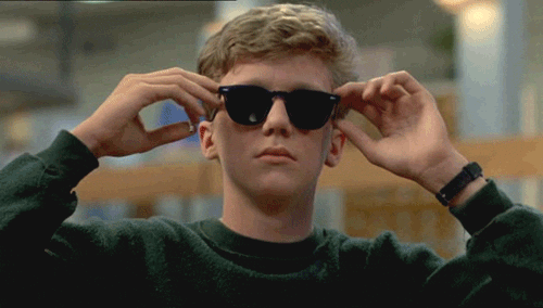 Movie gif. Anthony Michael Hall as Brian Johnson from the Breakfast Club adjusts his ray-ban sunglasses and shimmies.