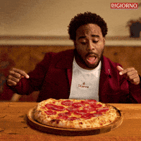 Sponsored gif. Man excitedly points to a pepperoni pizza in front of him with both hands. Flames erupt behind him. Text reads, “Fuego.”