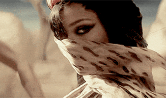 Celebrity gif. Rihanna stares dramatically from behind a scarf at us as the wind blows it past her face.