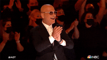 Reality TV gif. Howie Mandel on America's Got Talent gives a quick clap then smiles as he leans back and points with one arm extended.
