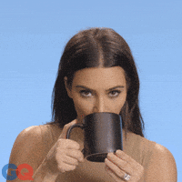 Celebrity gif. Kim Kardashian looks at us as she sips tea from a cup.