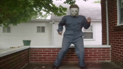 Movie gif. Nick Castle as Michael Myers dances energetically on a porch, swinging his knife around.