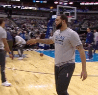Sports gif. Deron Williams from the Dallas Mavericks walks up to a child on the sidelines and gives him a low high five after completing a successful run.