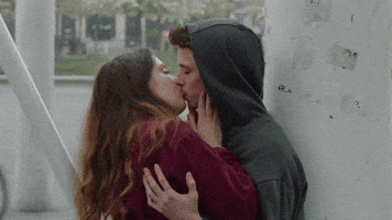 TV gif. Willem Herbots as Robbe and Zoe Schools as Maud from W T Fock, kissing passionately outside against a wall.