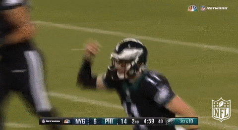 Sports gif. Carson Wentz in an Eagles football uniform holds his hand on his helmet and sprints down the field.