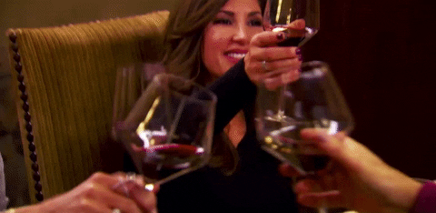 Reality TV gif. The cast of The Real Housewives Of New Jersey all cheer and clink wine glasses together.