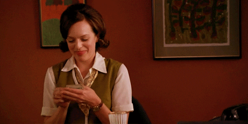 TV gif. Elisabeth Moss as Peggy from Mad Men smiles as she counts a pile of bills clutched in her hands. 