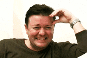 Celebrity gif. Ricky Gervais shakes with laughter. He squints and covers his eyes.