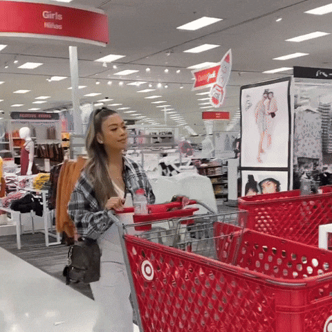 A woman shopping in a retail store, pushing a red shopping cart.