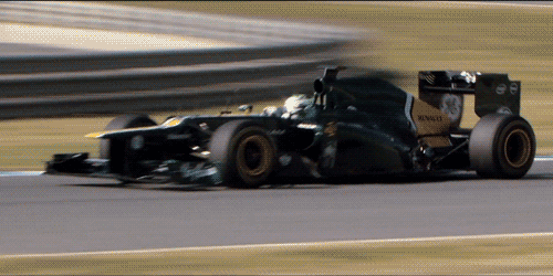 Sports gif. Green and gold F1 Caterham Renault Livery races toward us on a track, smoothly taking a turn.