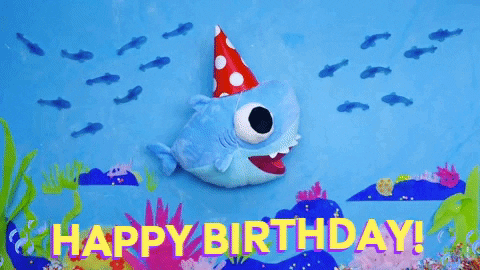 Digital illustration gif. Baby Shark stuffie swims across the bottom of the ocean floor wearing a red and white polka dot birthday hat that slides on and off its head. He's edited to look like his fins are moving as he bobs up and down in the water, giving the appearance of swimming. Fish pass by and bubbles emerge from the bottom. Text, "Happy Birthday!'