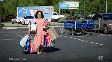 TV gif. Kaliko Kauahi as Sandra from Superstore looks overencumbered walks through a parking lot with her hands full of shopping bags. She drops some bags and stops, staring at them on the ground.